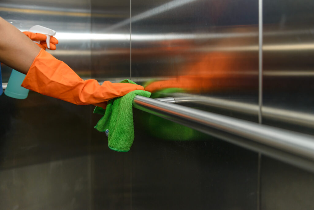 Woman hand in protective orange rubber gloves holding green microfiber cleaning cloth and wiping dust using a spray sterilizing solution make cleaning and disinfection for good hygiene